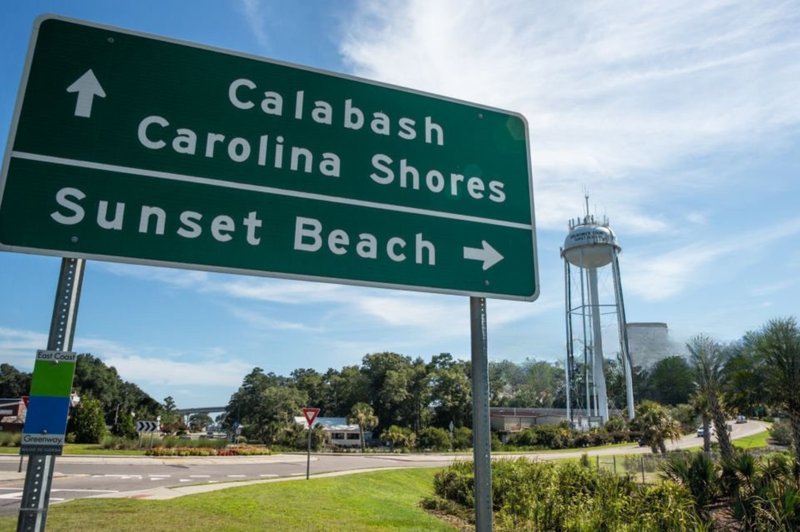 Road sign pointing to Calabash and Sunset Beach with water tower in the background in Calabash, NC